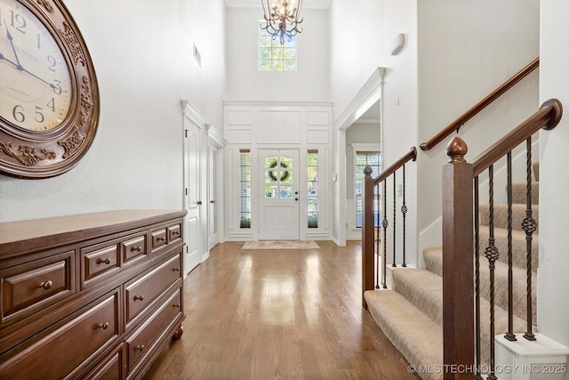 foyer with visible vents, wood finished floors, a chandelier, a towering ceiling, and stairs