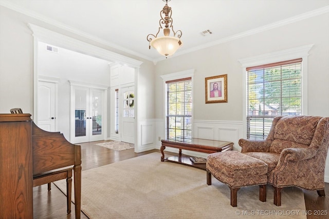 living area with a wainscoted wall, wood finished floors, visible vents, and ornamental molding