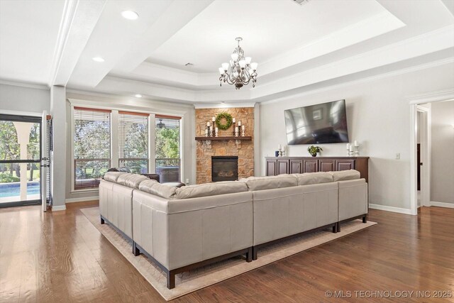 living area with a notable chandelier, ornamental molding, wood finished floors, a fireplace, and a raised ceiling