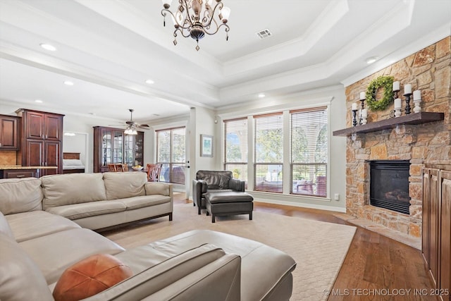 living room featuring crown molding, a tray ceiling, a stone fireplace, and light wood-type flooring