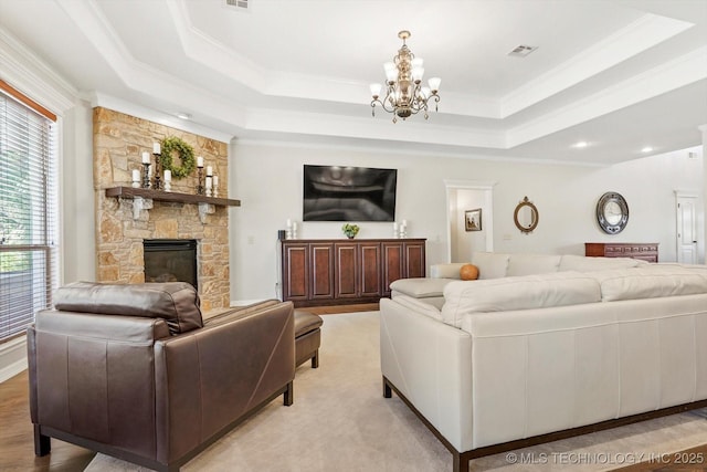 living room with visible vents, ornamental molding, a stone fireplace, a raised ceiling, and a chandelier
