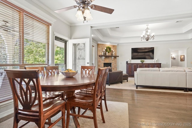 dining space featuring a tray ceiling, a fireplace, light wood-style floors, crown molding, and ceiling fan with notable chandelier