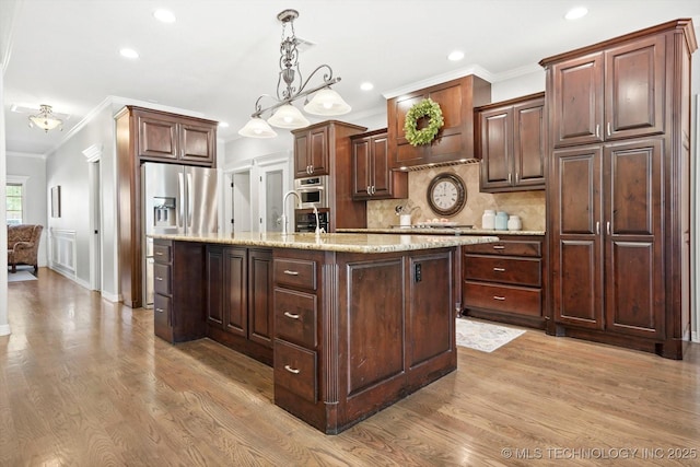 kitchen with crown molding, light wood-style floors, a kitchen island with sink, and backsplash