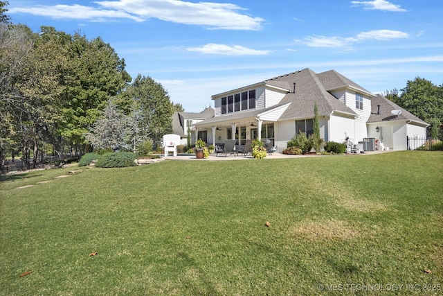 rear view of house with central AC unit, a lawn, a patio, and roof with shingles