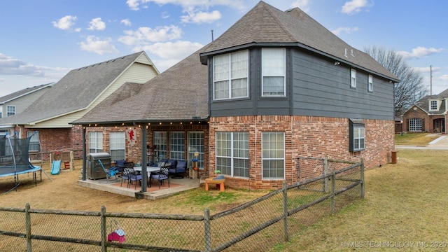 back of property with a trampoline, a patio area, and a lawn