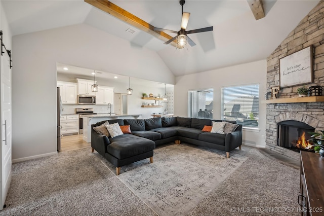 carpeted living room with ceiling fan, beam ceiling, high vaulted ceiling, a stone fireplace, and a barn door