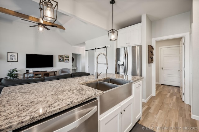 kitchen with sink, stainless steel appliances, light stone counters, white cabinets, and a barn door