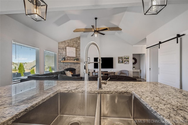 kitchen featuring a stone fireplace, lofted ceiling, ceiling fan, light stone counters, and a barn door