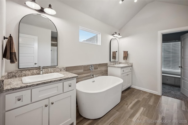 bathroom with vanity, vaulted ceiling, hardwood / wood-style floors, and a washtub