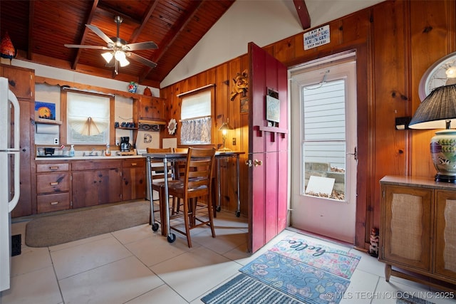 kitchen with lofted ceiling with beams, light tile patterned floors, wooden ceiling, and wood walls