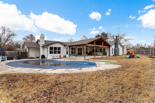 rear view of property with a playground, a covered pool, and a patio area