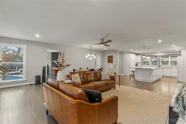 living room with ceiling fan with notable chandelier and light hardwood / wood-style floors