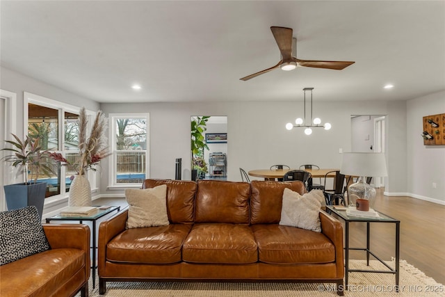 living room with ceiling fan with notable chandelier and light hardwood / wood-style flooring