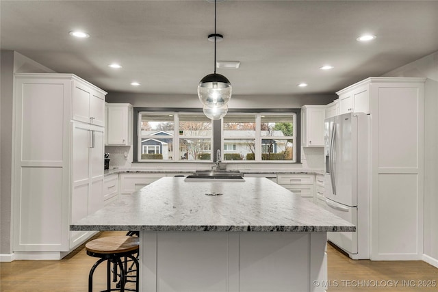 kitchen featuring hanging light fixtures, light hardwood / wood-style floors, white fridge with ice dispenser, white cabinets, and a kitchen island