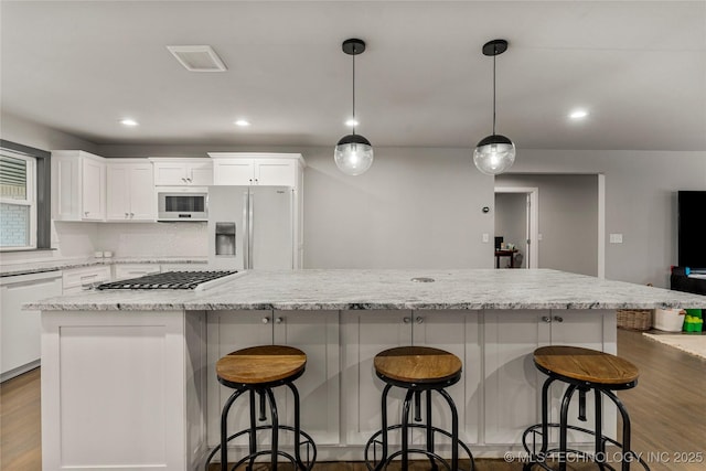 kitchen with a kitchen island, a breakfast bar, pendant lighting, white cabinets, and white appliances