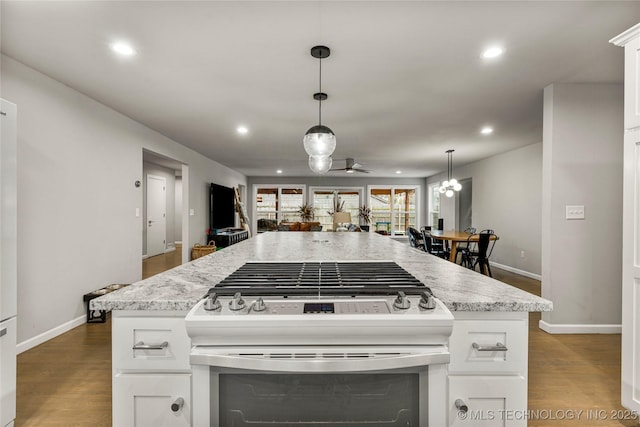 kitchen with hanging light fixtures, stainless steel range with gas cooktop, hardwood / wood-style floors, and white cabinets