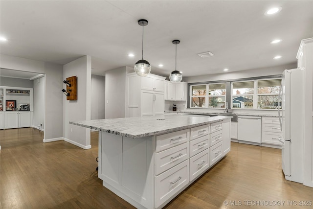 kitchen featuring pendant lighting, white appliances, a center island, light stone counters, and white cabinets