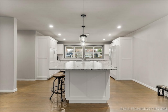 kitchen featuring pendant lighting, white cabinetry, light stone counters, white fridge with ice dispenser, and a kitchen island