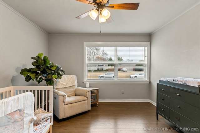 bedroom with dark wood-type flooring, ceiling fan, crown molding, and a crib