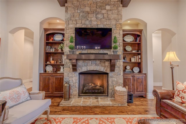 living room with built in shelves, a stone fireplace, and light wood-type flooring