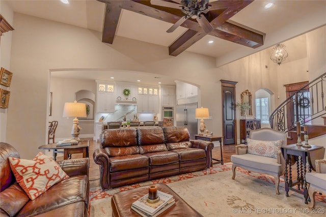 living room with a towering ceiling, ceiling fan with notable chandelier, and beam ceiling