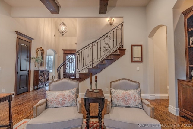 entryway featuring beamed ceiling, wood-type flooring, a high ceiling, and an inviting chandelier