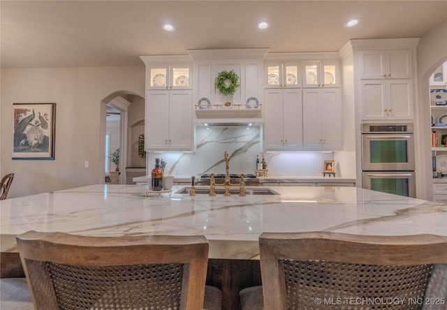 kitchen with light stone counters, stainless steel double oven, a kitchen breakfast bar, and white cabinets