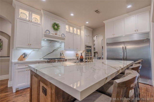 kitchen with light stone counters, an island with sink, white cabinets, and appliances with stainless steel finishes