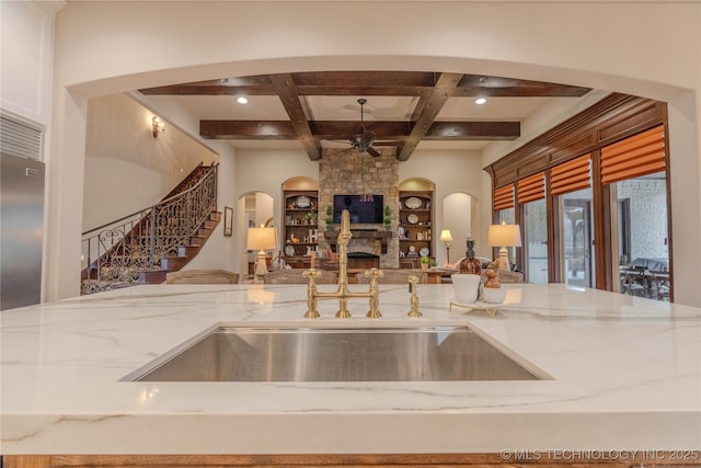 kitchen with light stone counters, ceiling fan, coffered ceiling, and a stone fireplace