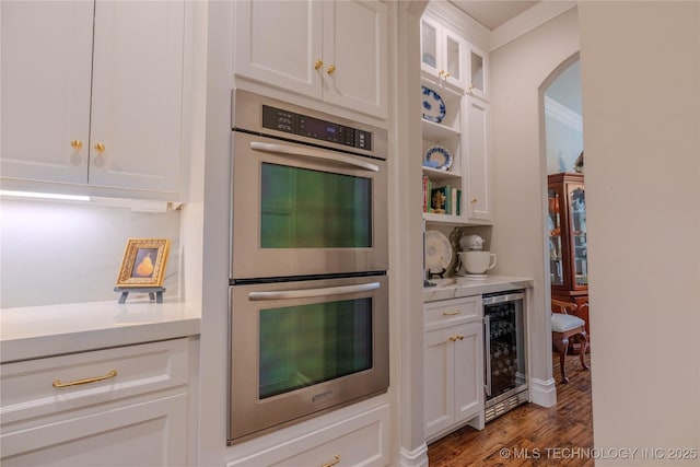 kitchen with double oven, white cabinetry, wine cooler, dark hardwood / wood-style flooring, and crown molding