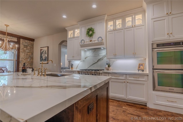 kitchen featuring hanging light fixtures, sink, stainless steel double oven, and white cabinets