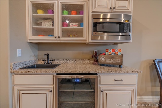 kitchen with stainless steel microwave, cream cabinets, sink, wine cooler, and light stone countertops