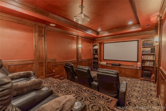 carpeted cinema room featuring ornamental molding, a tray ceiling, and built in features