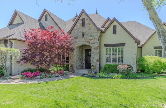 view of front of home with brick siding, a front lawn, a shingled roof, and stone siding