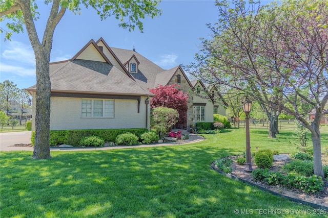 view of front of home with brick siding, a front lawn, fence, and roof with shingles