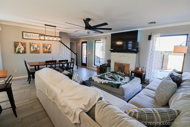 living room featuring hardwood / wood-style flooring, ceiling fan, ornamental molding, and a brick fireplace