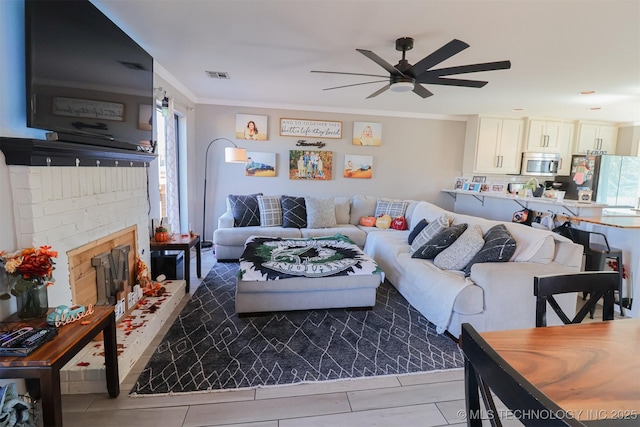 living room with a brick fireplace, crown molding, and ceiling fan