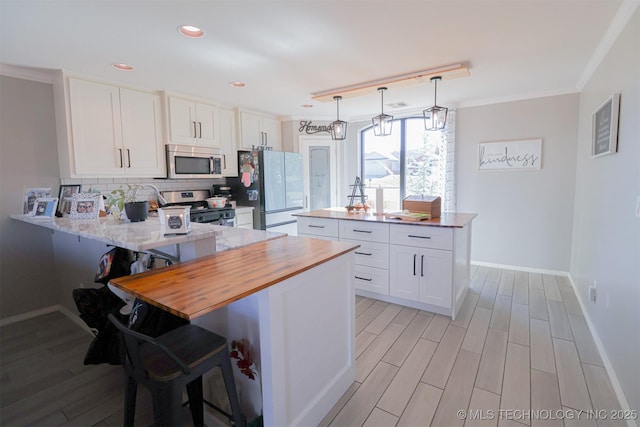 kitchen with white cabinetry, appliances with stainless steel finishes, a kitchen breakfast bar, and kitchen peninsula