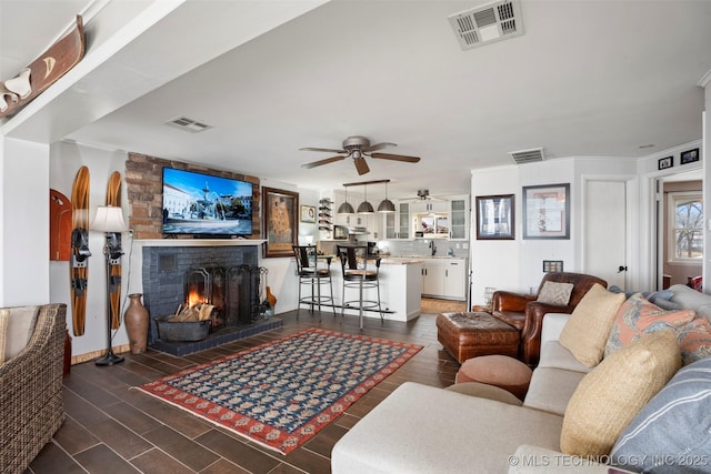 living room featuring a large fireplace, dark wood-type flooring, and ceiling fan