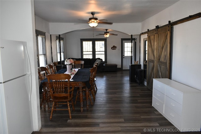 dining room with dark wood-type flooring, a barn door, and ceiling fan