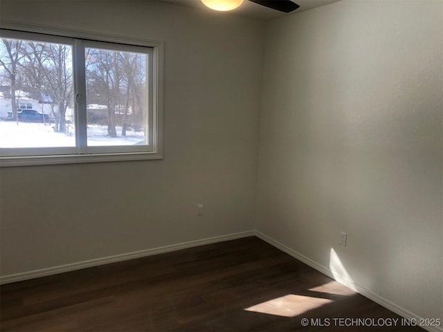 spare room with dark wood finished floors, a ceiling fan, and baseboards