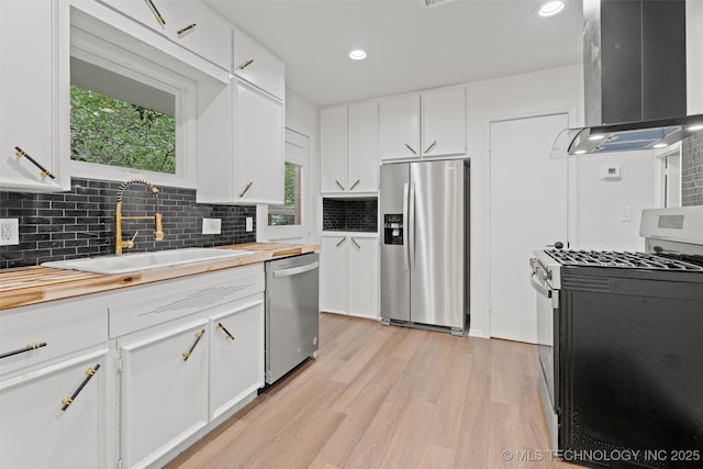 501 W 17th St, Pawhuska, OK 74056 - kitchen featuring appliances with stainless steel finishes, wall chimney range hood, wooden counters, a sink, and light wood-style floors