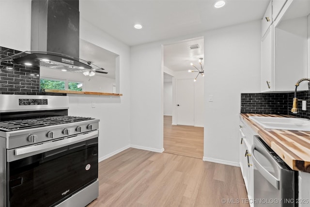 501 W 17th St, Pawhuska, OK 74056 - kitchen with appliances with stainless steel finishes, range hood, wooden counters, a sink, and white cabinetry