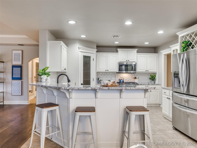 kitchen with a breakfast bar, light stone counters, tasteful backsplash, stainless steel appliances, and white cabinets