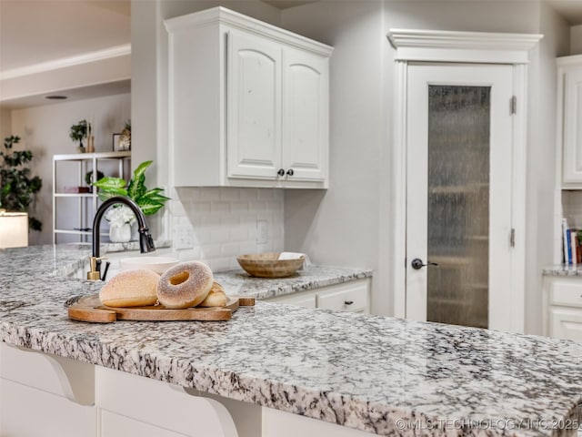 kitchen with backsplash, light stone countertops, sink, and white cabinets