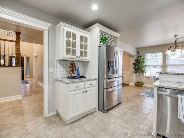 kitchen featuring appliances with stainless steel finishes, white cabinetry, hanging light fixtures, light stone countertops, and decorative backsplash