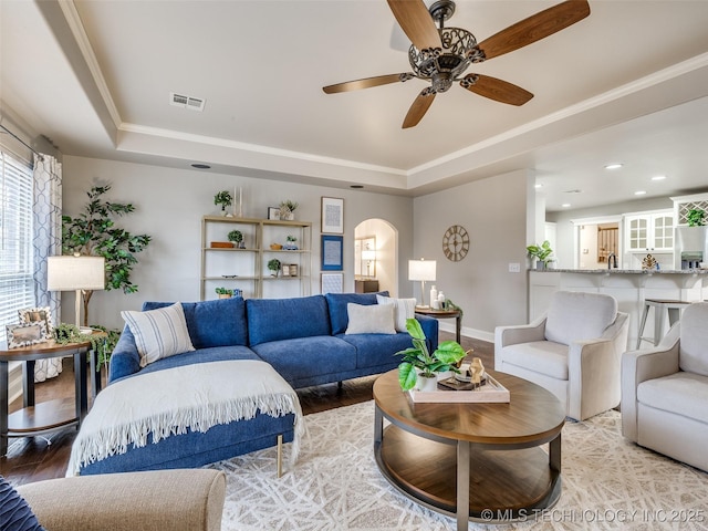 living room with crown molding, a tray ceiling, and wood-type flooring