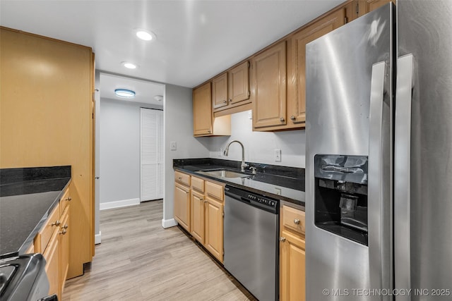 kitchen with appliances with stainless steel finishes, sink, dark stone countertops, and light hardwood / wood-style floors