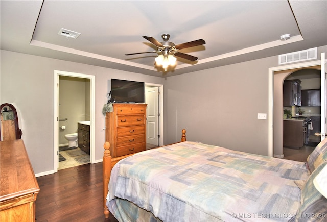 bedroom with ensuite bathroom, dark wood-type flooring, ceiling fan, and a tray ceiling