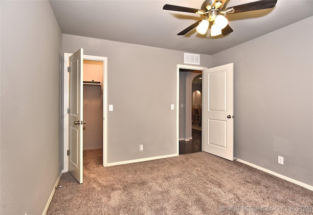 unfurnished bedroom featuring a walk in closet, a closet, ceiling fan, and carpet